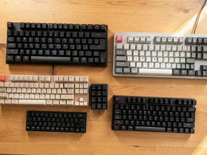 Several mechanical keyboards of different sizes arranged on a wooden desk