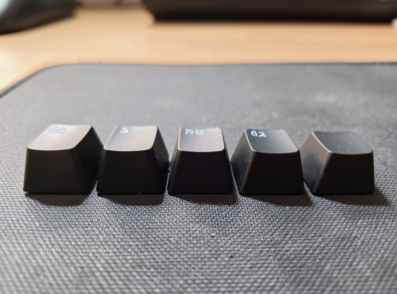Several keycap sets in different profiles arranged on a desk mat showing height and sculpt differences