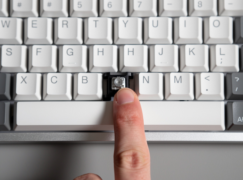 Pressing each corner of a reinstalled spacebar to check it sits level