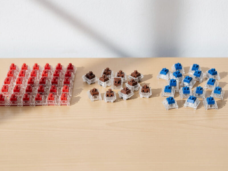 Red linear, brown tactile, and blue clicky mechanical keyboard switches grouped on a desk