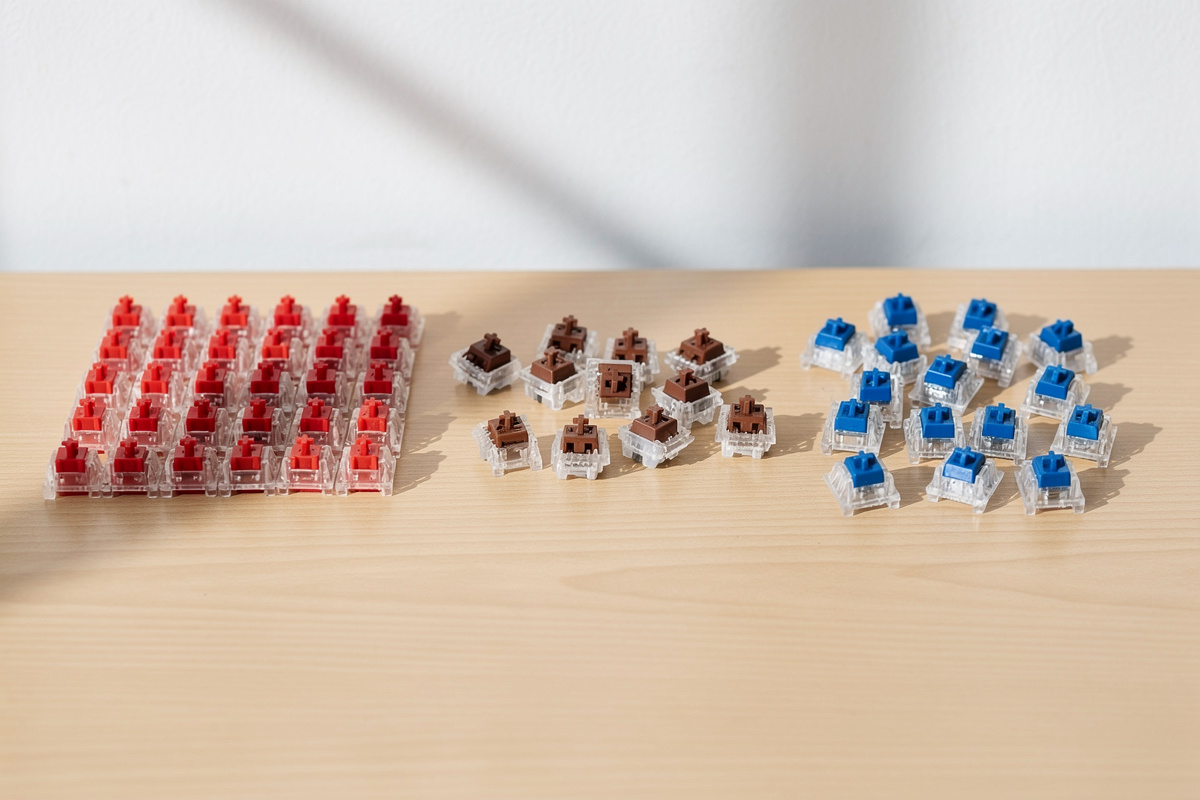Red linear, brown tactile, and blue clicky mechanical keyboard switches grouped on a desk