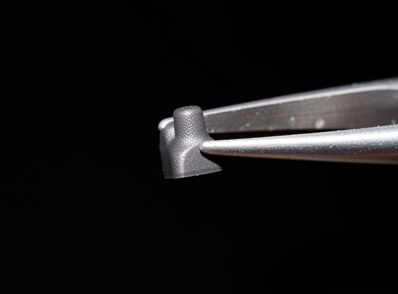 Macro of a tactile keyboard switch stem held in tweezers showing the tactile bump on the leg