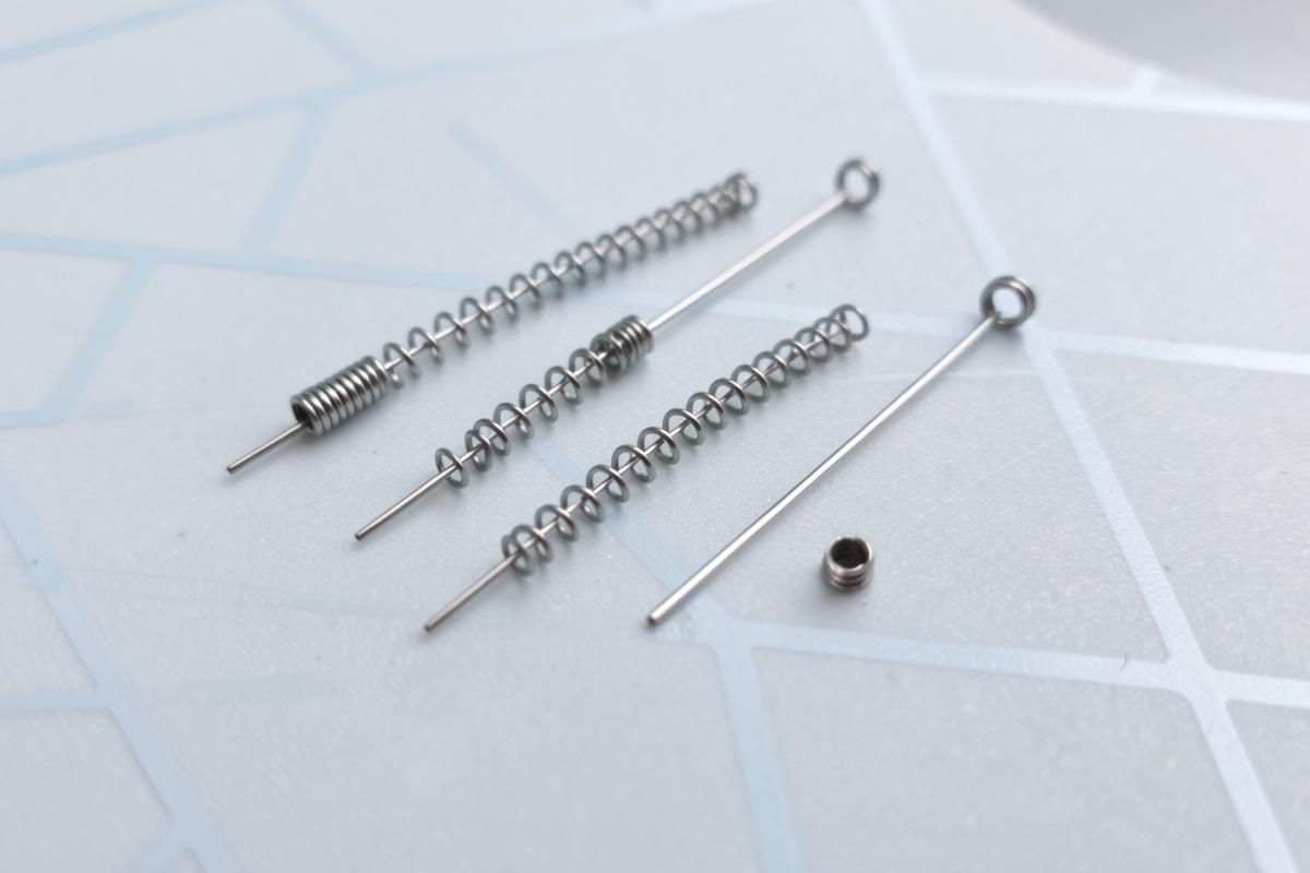 A close-up of keyboard switch springs of different lengths laid out on a desk mat