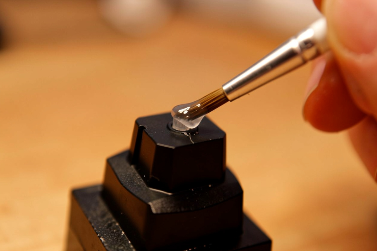 A small brush applying a thin film of grease to a switch stem held in a stem holder