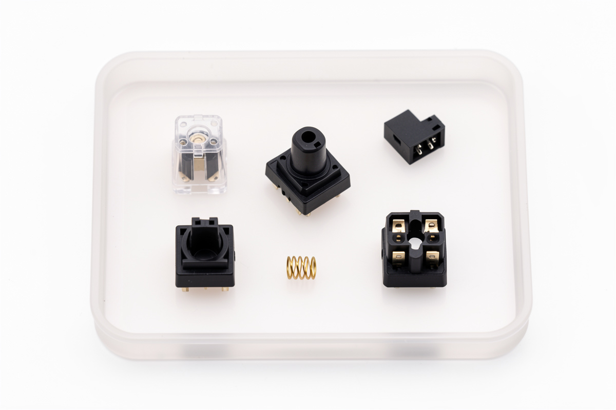 A keyboard switch disassembled into stem, top housing, bottom housing and spring on a lube station tray